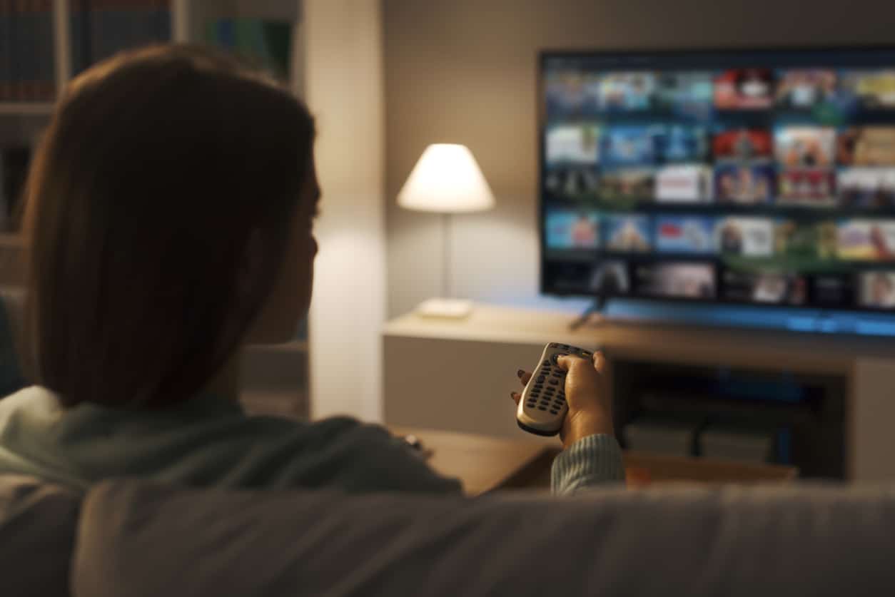 Young woman relaxing on the couch at home and watching videos on demand on her TV, entertainment concept